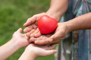 The red rubber heart on hands of elderly and child. Showed the cooperate, love, care, charity of people with differences diversity for sustain develop of farmer, community, society and the environment